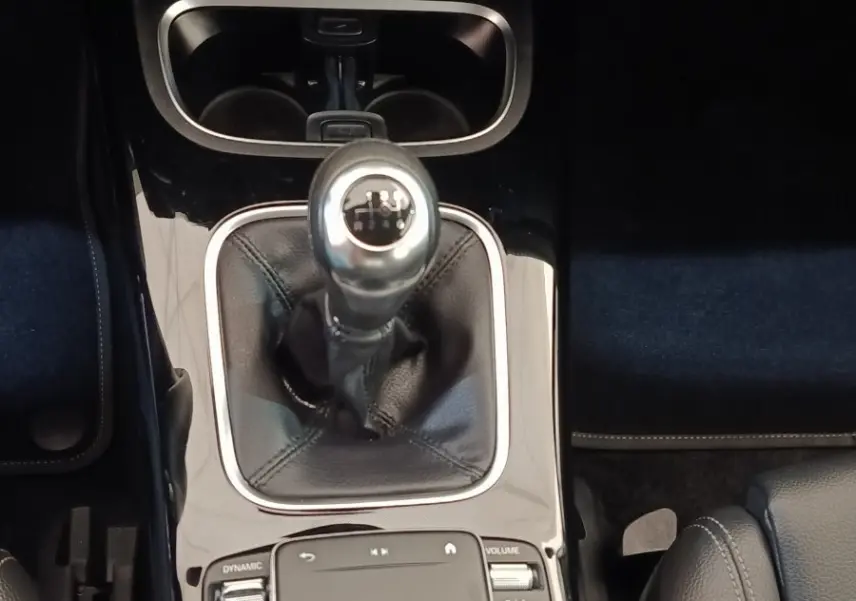 Vue rapprochée de la console centrale noire brillante avec levier de vitesses manuel et commandes tactiles d’une Mercedes Classe A gris clair.