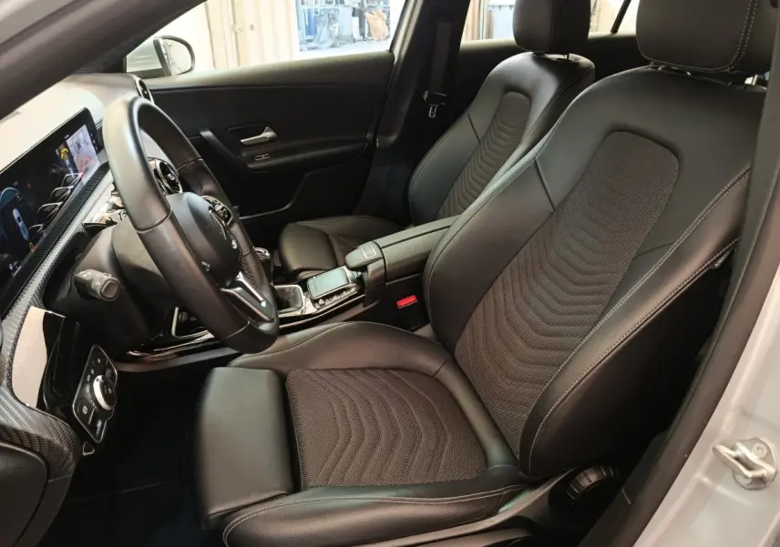 Vue intérieure côté conducteur de la Mercedes Classe A 180 d Business Line 2021 avec sièges cuir noirs et volant multifonctions.