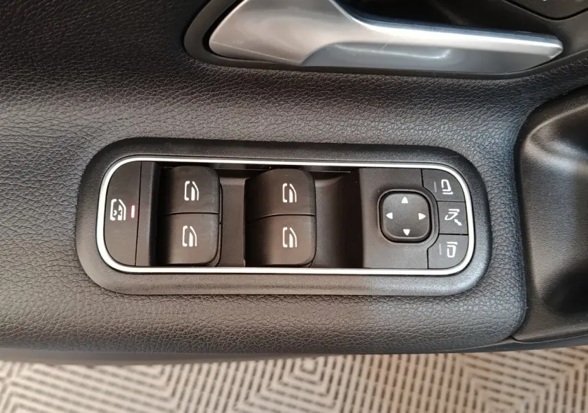 Gros plan sur les commandes des vitres électriques et rétroviseurs sur la porte côté conducteur d’une Mercedes Classe A gris clair.