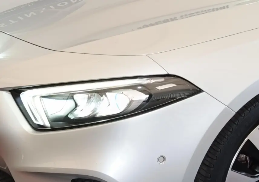 Gros plan sur l'avant droit gris clair d'une Mercedes Classe A 180 d Business Line avec phare LED allumé.