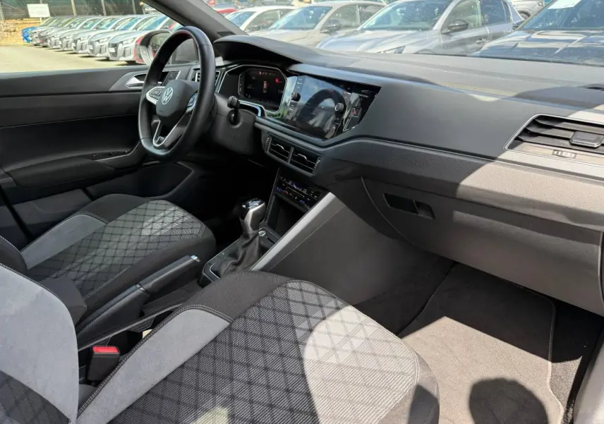Vue intérieure côté conducteur du Volkswagen Taigo 2025, sièges tissu R-Line gris avec motifs, tableau de bord moderne noir.