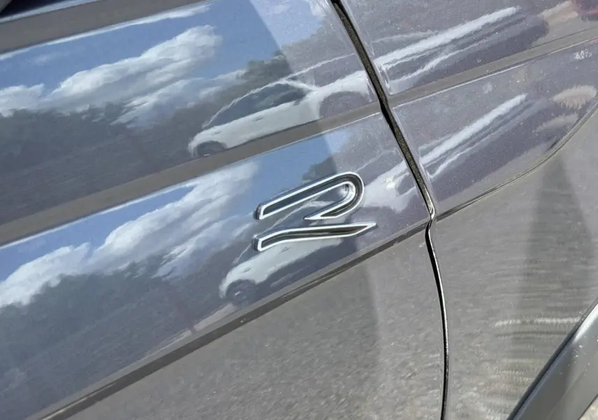 Détail sur la portière arrière droite grise du Volkswagen Taigo 1.0 TSI 116ch R-Line avec reflet et logo "R".