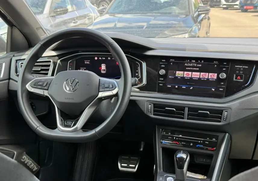 Vue intérieure avant du Volkswagen Taigo gris 2025, volant cuir multifonction et écran tactile central allumé.