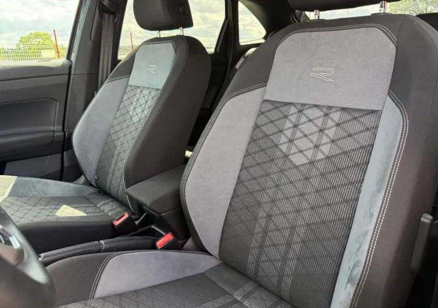 Vue intérieure rapprochée des sièges avant gris R-Line avec motifs géométriques et accoudoir central du Volkswagen Taigo 2025.