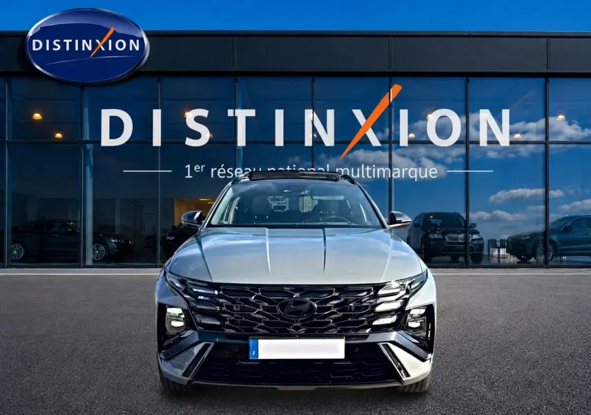 Vue frontale du Hyundai Tucson gris shadow 2026 avec calandre noire et feux LED distinctifs, devant une vitrine Distinxion.