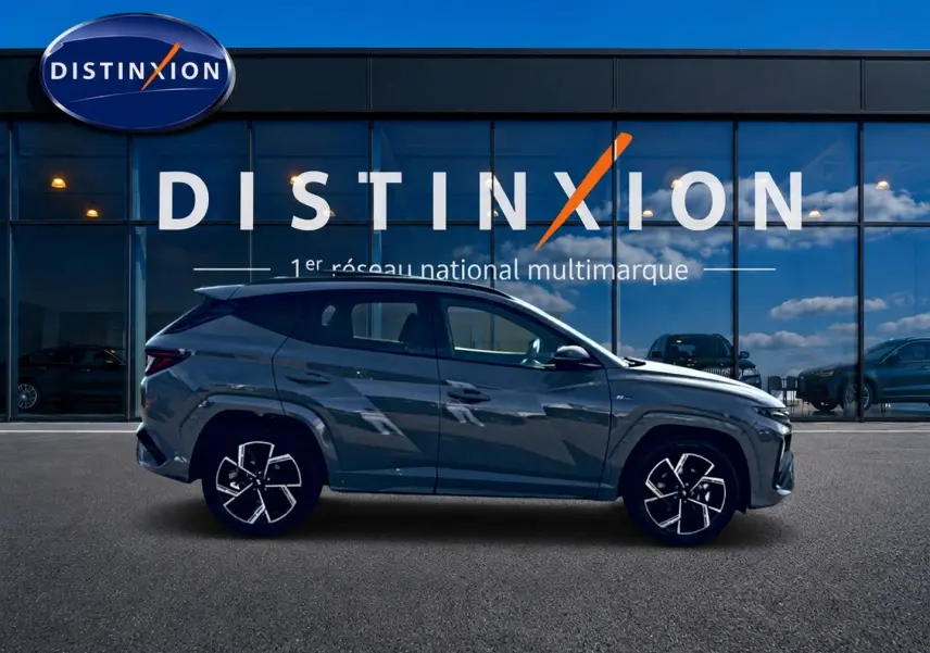 Hyundai Tucson 2026 gris shadow en profil gauche devant vitrine Distinxion, avec jantes alu et lignes marquées.