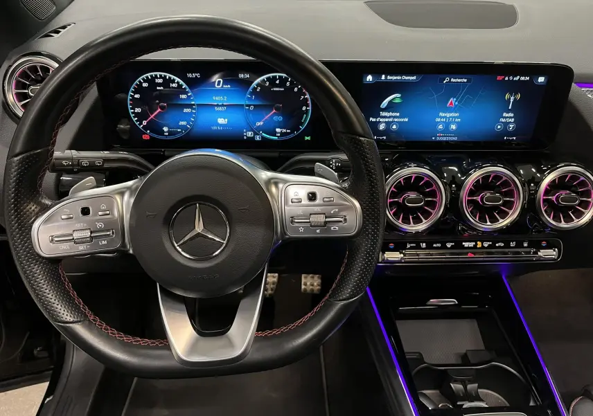 Vue intérieure centrée sur le volant noir avec surpiqûres rouges et tableau de bord numérique du Mercedes GLA 250E AMG Line.