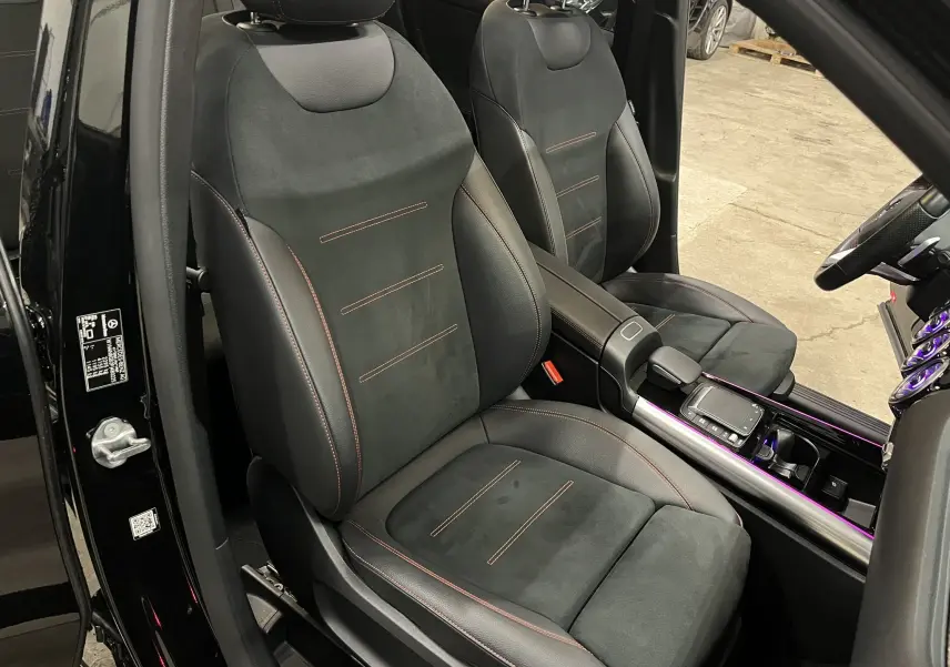 Vue intérieure rapprochée des sièges avant noirs avec surpiqûres rouges et console centrale illuminée d’un Mercedes GLA 250E AMG Line.