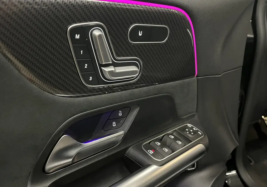 Détail de la porte côté gauche du Mercedes GLA 250E AMG Line 2023, avec commandes sièges, surpiqûres rouges et éclairage d'ambiance violet.