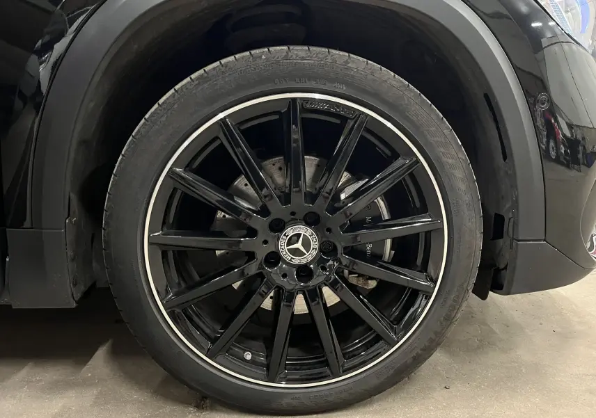 Gros plan sur la roue avant gauche noire brillante du Mercedes GLA 250E AMG Line avec jante à rayons fins et logo Mercedes central.