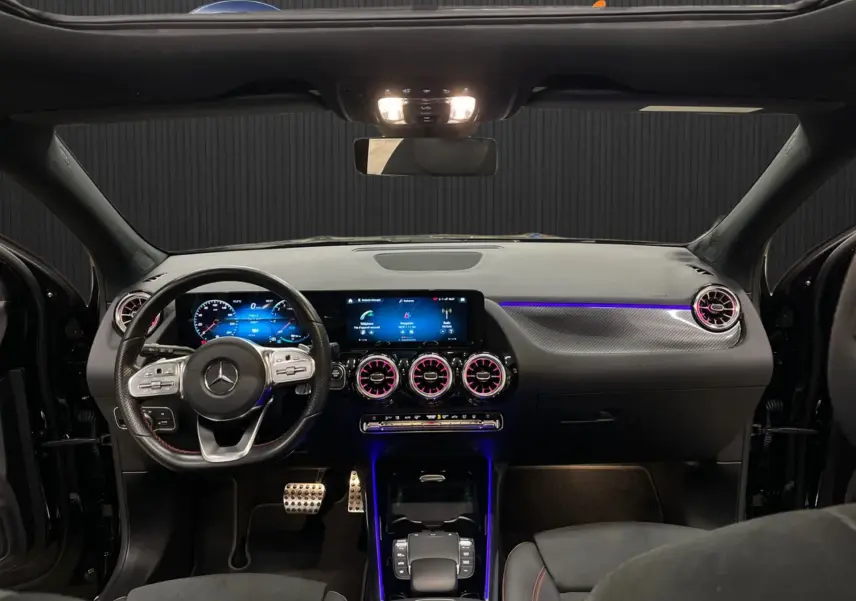 Vue intérieure avant du Mercedes GLA 250E AMG Line 2023 noir, avec éclairage d'ambiance violet et surpiqûres rouges.