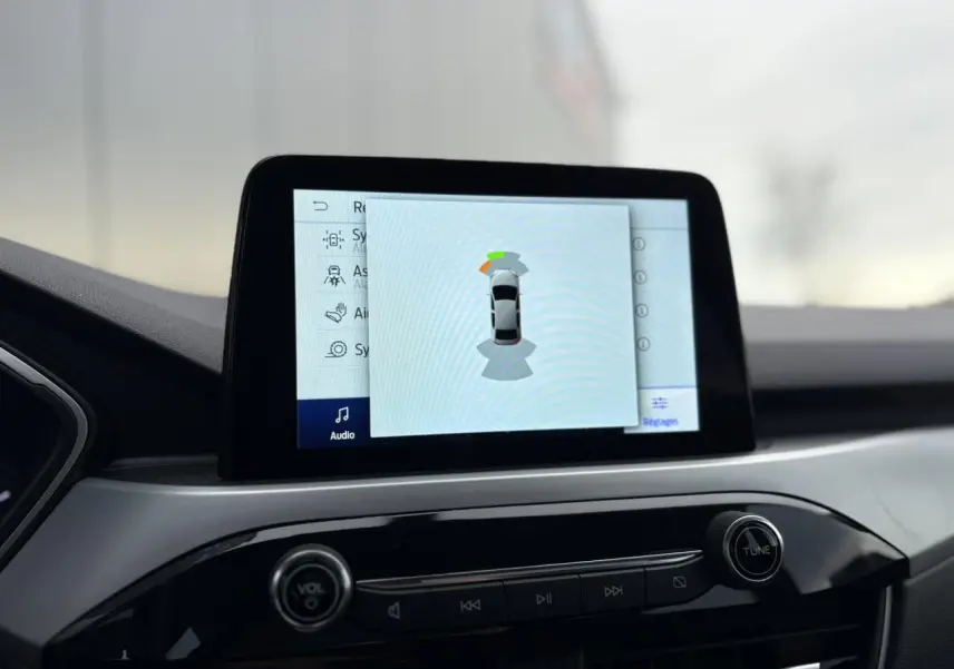 Écran tactile central du Ford Kuga 2024 affichant l’aide au stationnement avec vue sur la console noire brillante.