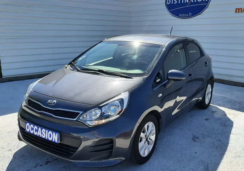 KIA Rio grise vue 3/4 avant droit, compacte 5 portes avec jantes alliage et plaque "OCCASION" visible.