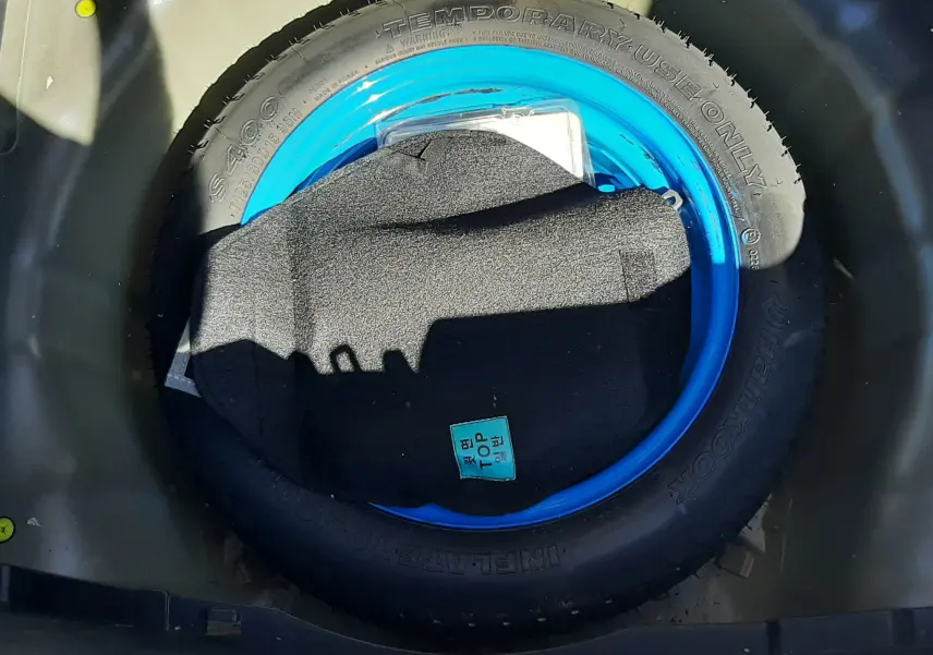 Gros plan sur la roue de secours bleue dans le coffre d'une KIA Rio grise 2016, version essence 1.2 85CH ACTIVE.