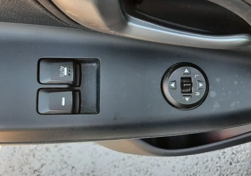 Gros plan sur les commandes de lève-vitres et réglage des rétroviseurs côté conducteur d'une Kia Rio grise 2016.