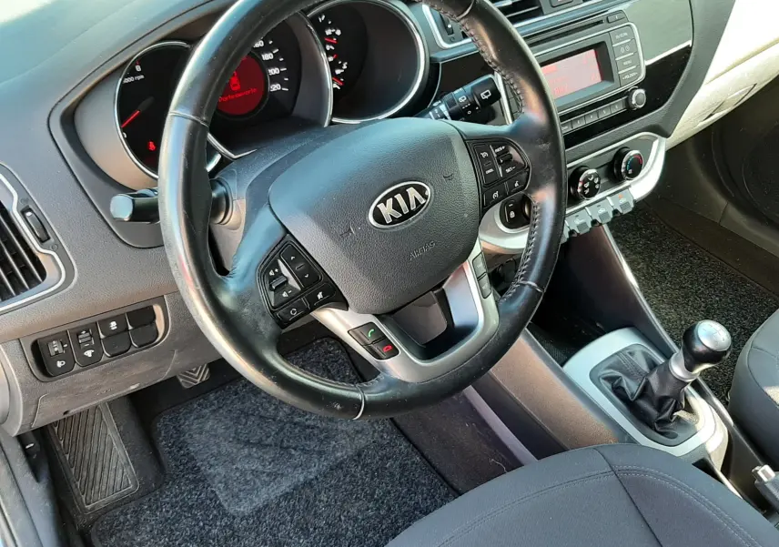 Vue intérieure côté conducteur de la Kia Rio grise 2016, volant multifonction et levier de vitesses manuel visibles.