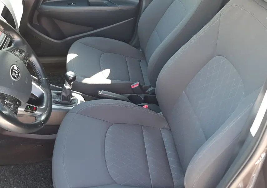 Vue intérieure côté conducteur de la Kia Rio grise 2016, montrant les sièges tissu gris et la boîte manuelle.