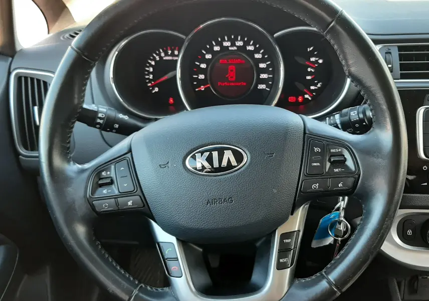 Vue rapprochée du volant noir de la KIA Rio 2016 avec tableau de bord et affichage digital rouge au centre.