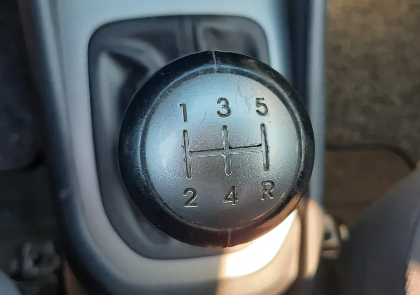 Gros plan sur le pommeau de la boîte manuelle 5 vitesses d'une KIA RIO grise, version 2016, intérieur tissu gris.
