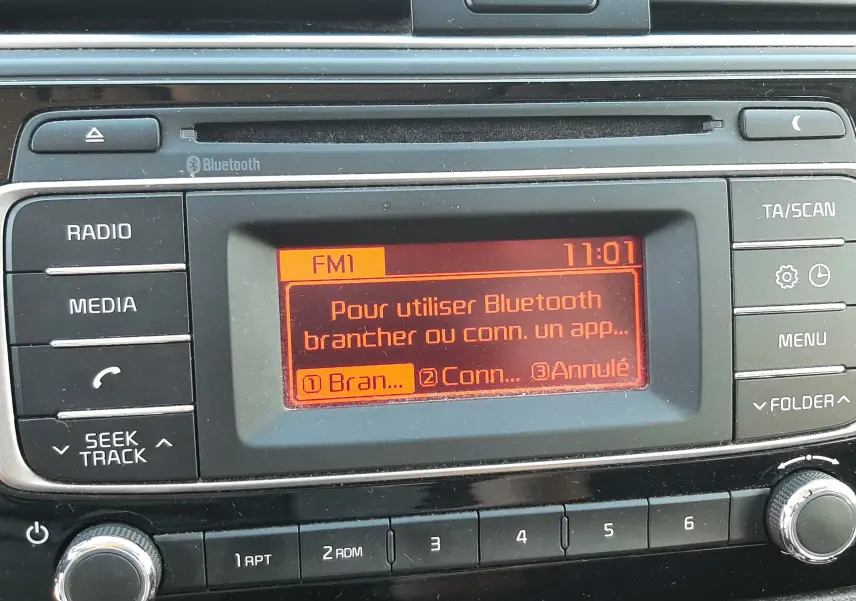 Gros plan sur l’écran central du tableau de bord de la Kia Rio grise 2016, affichant le menu Bluetooth en orange.