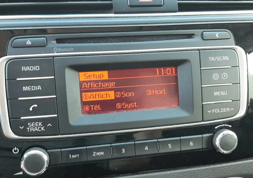 Gros plan sur la console centrale de la Kia Rio grise 2016, affichage radio orange avec boutons de commande autour.