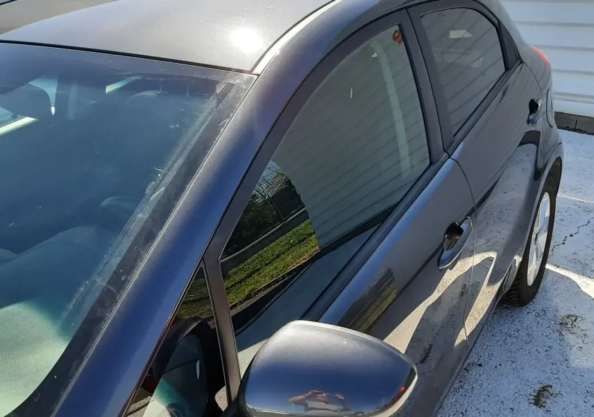 Vue 3/4 avant droit d'une KIA Rio grise 5 portes de 2016 avec rétroviseur électrique et vitres teintées.