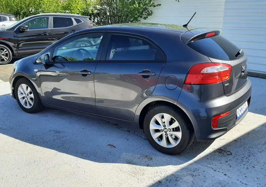 KIA Rio grise vue 3/4 arrière côté gauche, compacte 5 portes avec jantes alliage et feux arrière rouges.