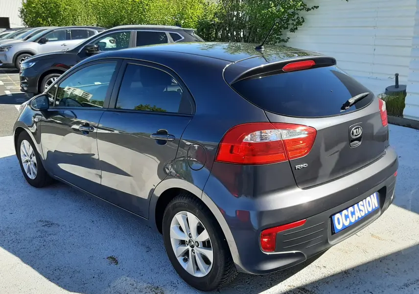 KIA Rio grise vue 3/4 arrière droit, compacte 5 portes avec feux arrière rouges et jantes alliage.