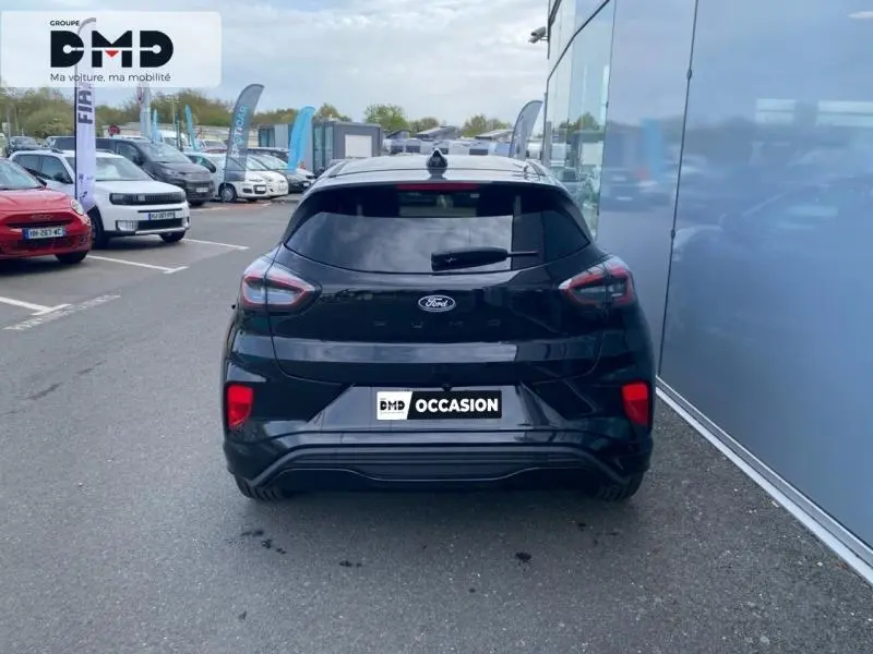 Vue arrière d'un Ford Puma noir Agate métallisé garé près d'un bâtiment vitré, avec feux arrière LED distinctifs.