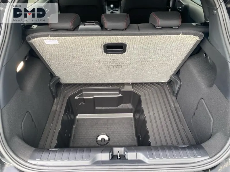 Coffre ouvert vu de l'arrière du Ford Puma noir, montrant le rangement sous plancher et banquette arrière avec surpiqûres rouges.