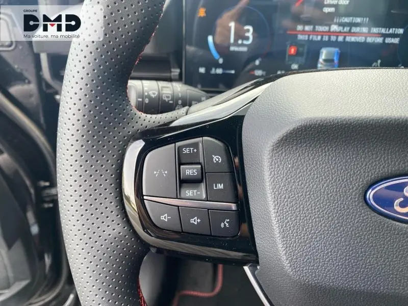 Gros plan sur le volant perforé noir du Ford Puma 2026, avec commandes multifonctions et tableau de bord numérique en arrière-plan.