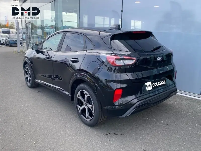 Vue 3/4 arrière droite d'un Ford Puma noir Agate métallisé avec jantes alu et feux arrière LED, stationné devant un bâtiment.