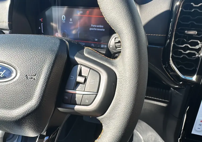 Vue rapprochée du volant cuir multifonctions noir du Ford Ranger Wildtrak 2026 avec tableau de bord digital allumé.