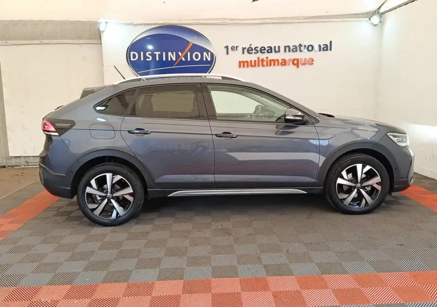 Vue de profil côté droit d'un Volkswagen Taigo gris foncé 2023 avec jantes alliage et barres de toit chromées.