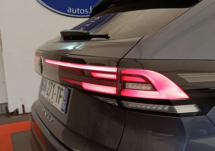 Vue arrière droite du Volkswagen Taigo gris foncé 2023 avec feux arrière LED allumés et logo visible.