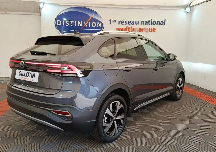 Volkswagen Taigo gris foncé en 3/4 arrière droit, avec feux arrière LED allumés dans un showroom.