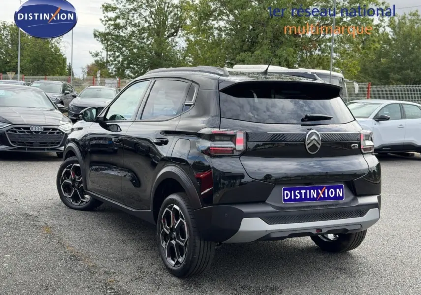 Vue 3/4 arrière d'une Citroën C3 noire 2025 avec jantes noires et détails rouges, stationnée en extérieur sur parking.