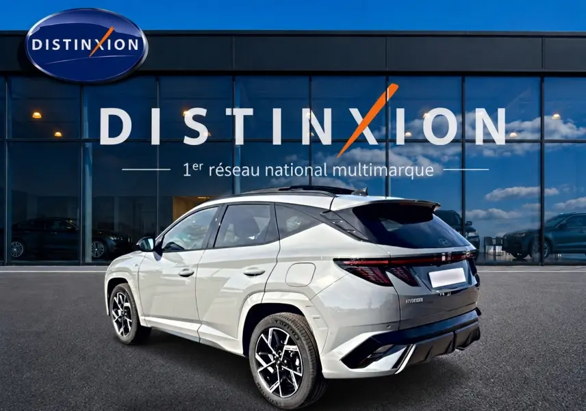 Vue 3/4 arrière droite du Hyundai Tucson 2026 gris shadow avec jantes alu et toit panoramique devant une vitrine Distinxion.