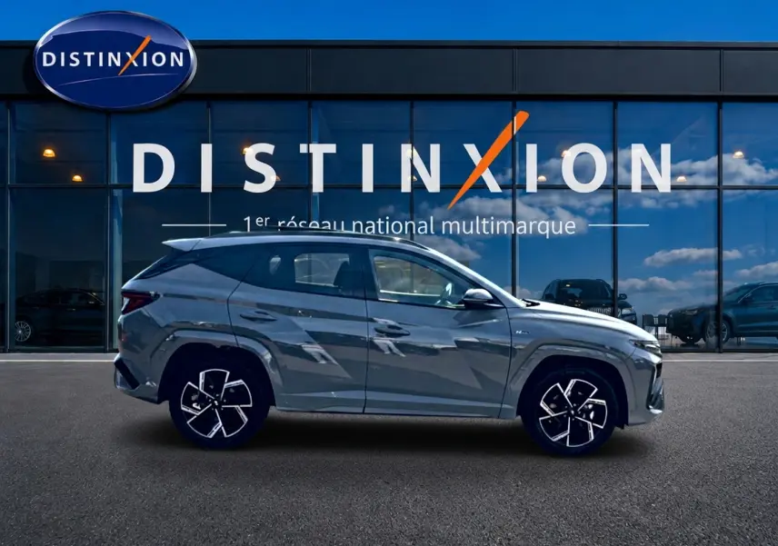 Hyundai Tucson 2026 gris shadow en profil droit devant une vitrine avec logo Distinxion.