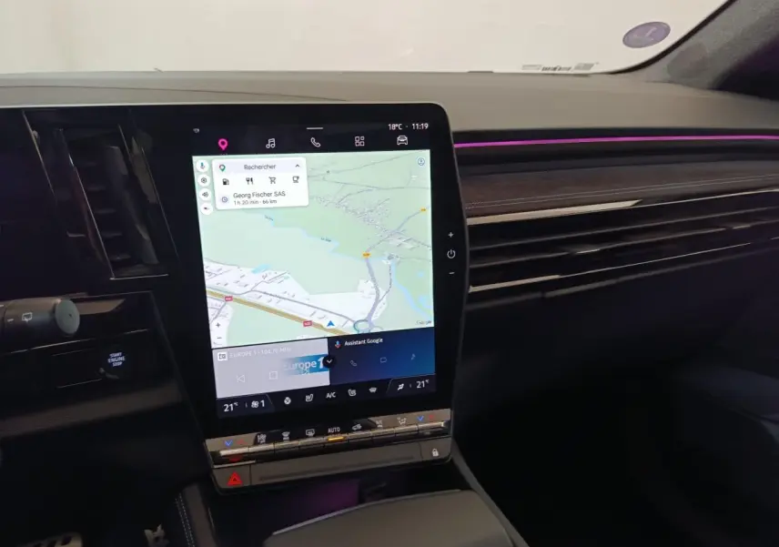 Vue intérieure du tableau de bord du Renault Austral gris clair, avec écran tactile central affichant la navigation et éclairage d’ambiance violet.