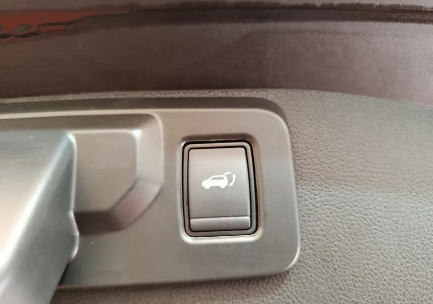 Bouton noir d'ouverture électrique du coffre sur panneau intérieur gris d'un Renault Austral gris clair, vue rapprochée.