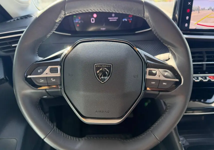 Vue rapprochée du volant cuir noir de la Peugeot 208 2025 avec commandes intégrées et logo lion central.