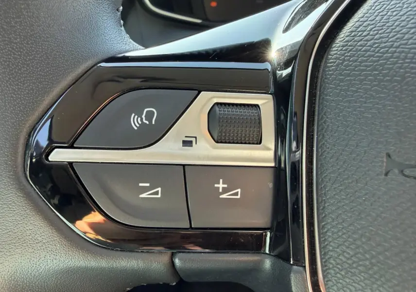 Gros plan sur les commandes audio au volant noir brillant de la Peugeot 208 1.2 100ch S&S Allure 2025.
