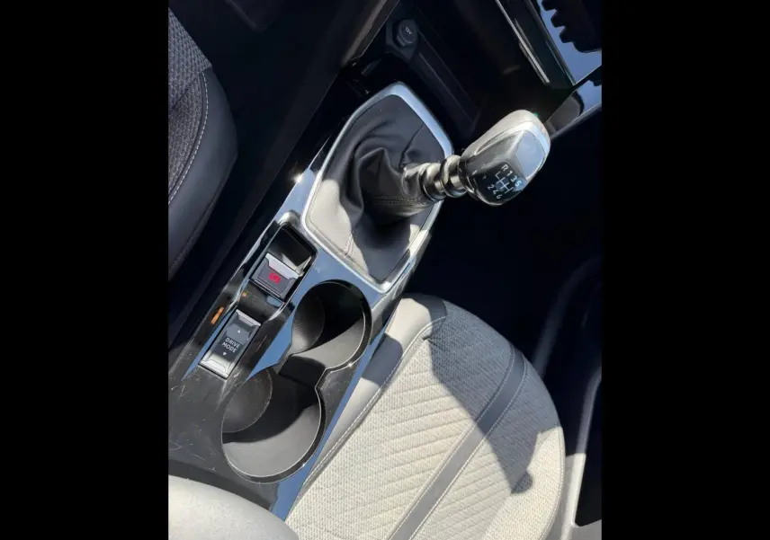Gros plan sur la console centrale intérieure de la Peugeot 208 2025, avec levier de vitesse manuel et siège tissu gris clair.