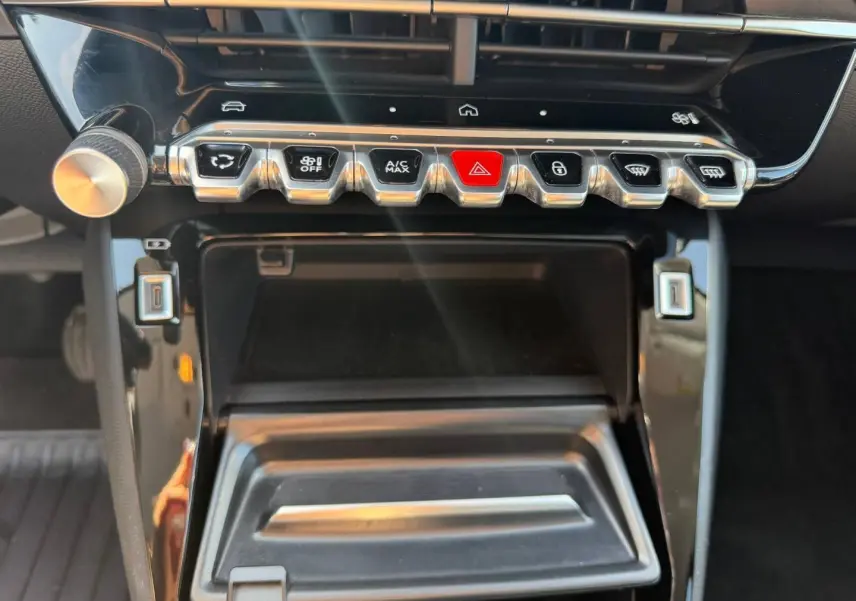 Gros plan sur la console centrale de la Peugeot 208 1.2 100ch Allure, montrant les commandes clim et rangement ouvert.
