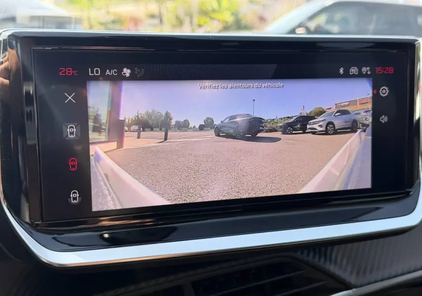 Écran tactile intérieur montrant la caméra de recul avec vue arrière sur un parking ensoleillé.