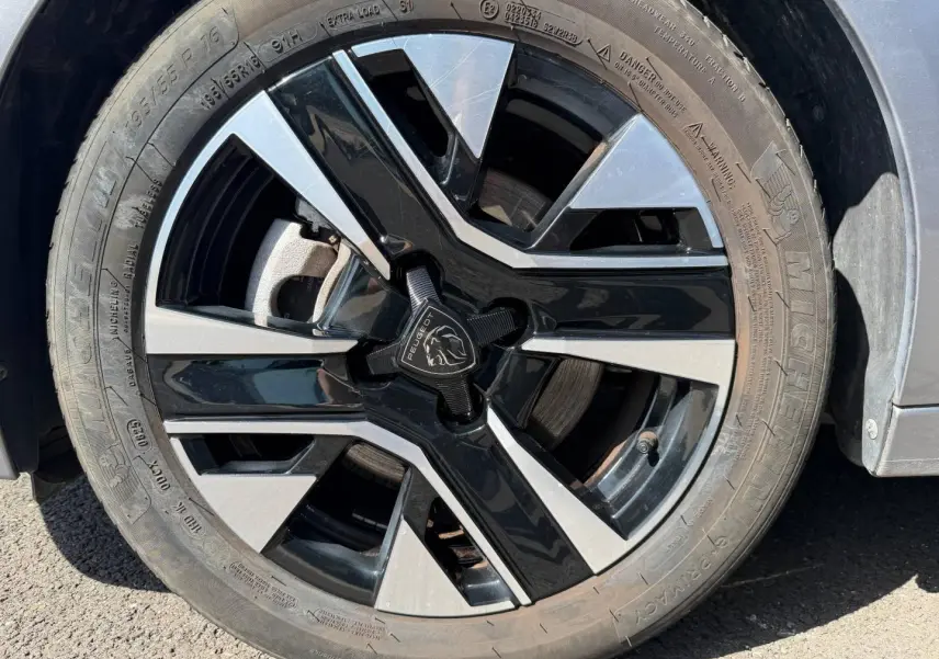 Gros plan sur la jante alu bicolore noire et argentée d'une Peugeot 208 Gris Artense, roue avant droite visible.