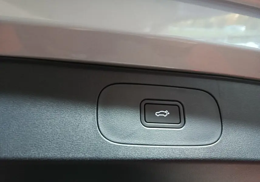 Gros plan sur le bouton d'ouverture électrique du coffre, entouré de plastique noir, sur un véhicule gris clair Geely STARRAY.