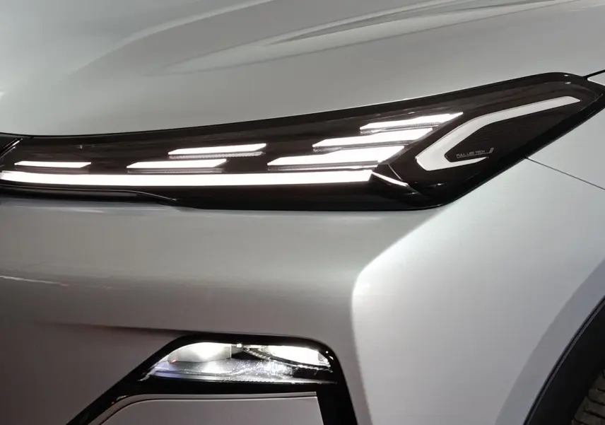 Gros plan sur le phare avant droit allumé d’un Geely STARRAY gris clair avec éclairage LED distinctif en bandeau.