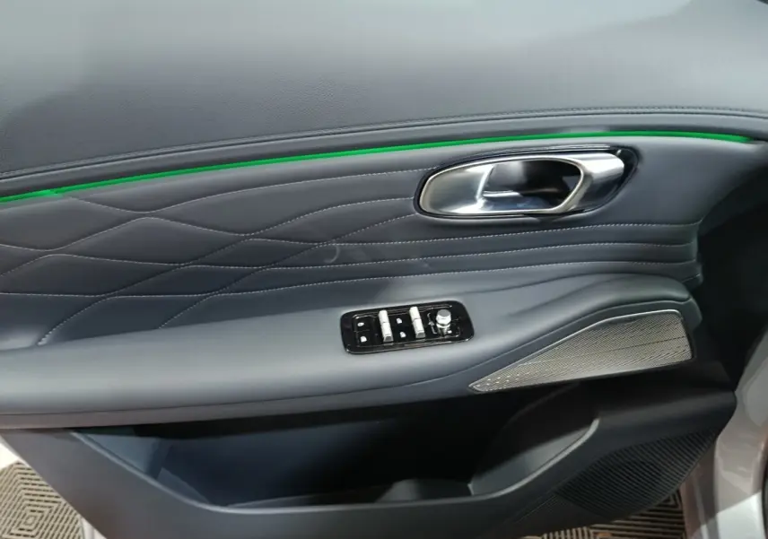 Gros plan sur la porte côté gauche gris clair du Geely STARRAY 2026, avec surpiqûres, bande lumineuse verte et commandes électriques.
